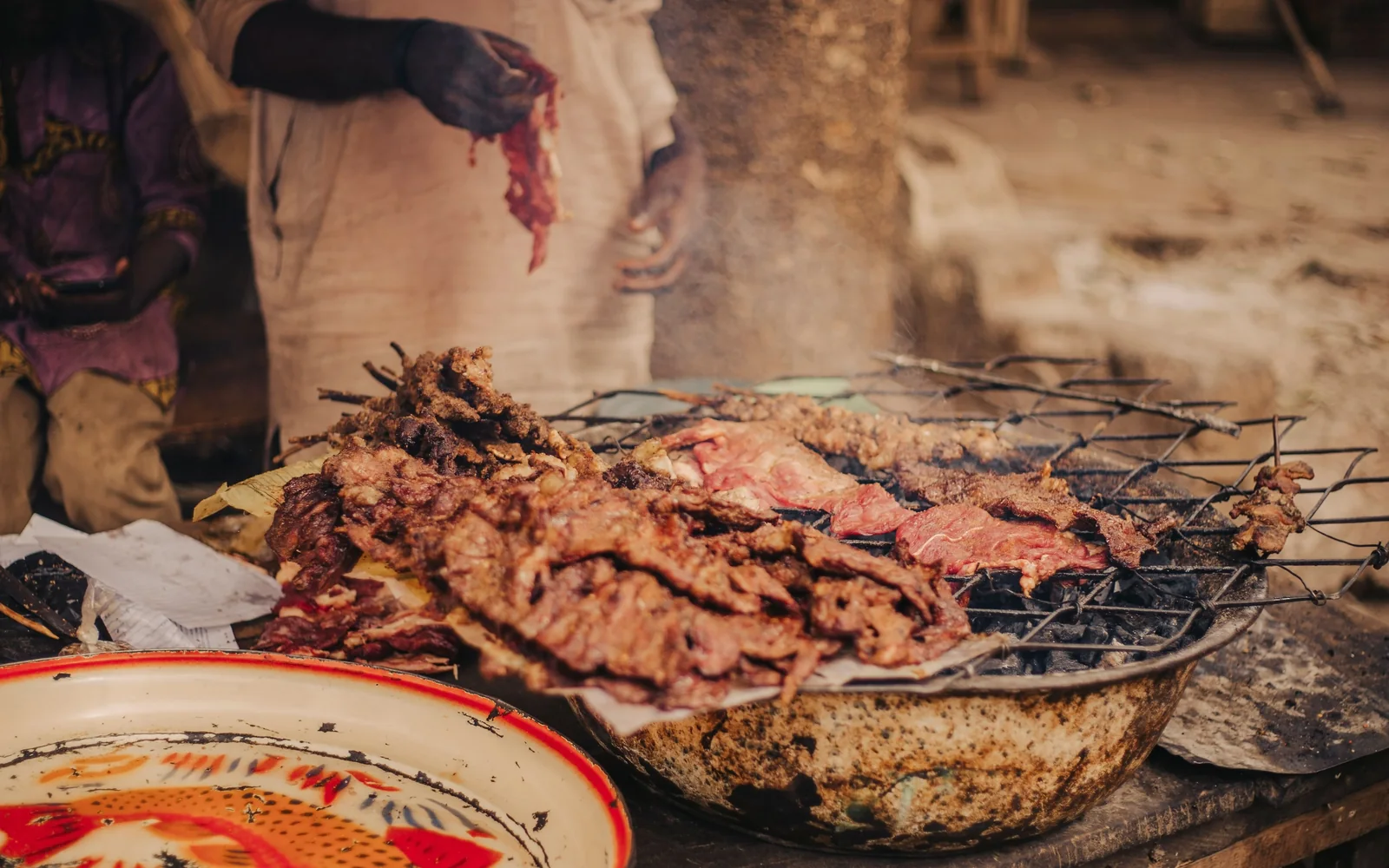 Grilled meat being carved and served from an open charcoal grill at a street food stall in Africa (representative photograph of nyama choma-style grilling, not Nyama Choma Ranch's own grill)